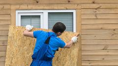 Worker nailing plywood over window of home