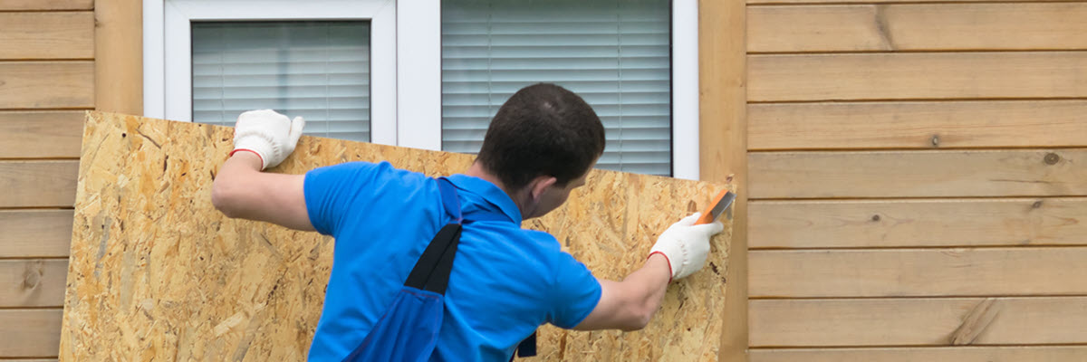 Worker nailing plywood over window of home